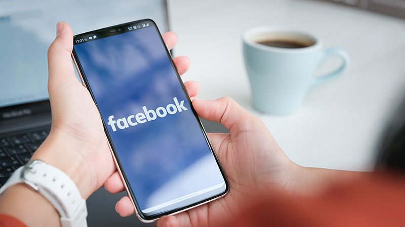 Persona con in mano uno smartphone che mostra la schermata dell'app Facebook